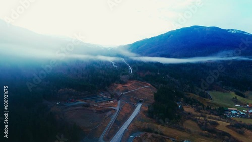 Scenic Aerial View of Mountains, Fjord, and Waterfall Set Amidst Trees and Rolling Clouds in a Breathtaking Wilderness
