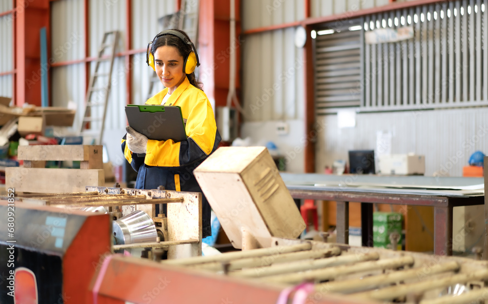 Industrial engineer in safety jacket working in heavy metal engineering factory. Confident Latin technician inspector woman worker check product quality in metalwork steel manufacturing facility. Industrial engineer in safety jacket working in heavy metal engineering factory. Confident Latin technician inspector woman worker check product quality in metalwork steel manufacturing facility.
