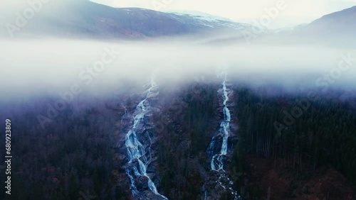 Aerial Panorama of Majestic Mountains, Waterfall, and Fjord Enveloped by Clouds and Green Forests in a Peaceful Natural Setting