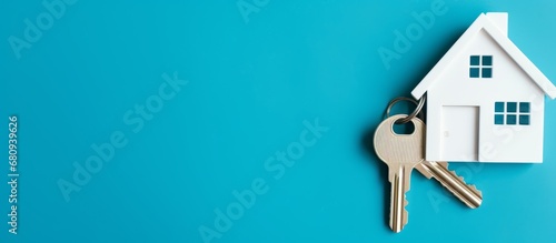 The concept of buying real estate, minimalistic blue background. A key with a keychain in the form of a house. Rental housing, purchase or sale. Banner with copy space. Generative AI. photo