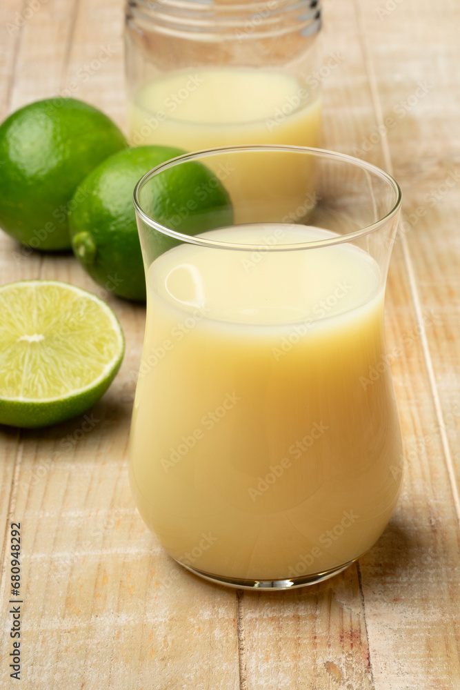 Drinking glass with lime juice and fresh green limes on the table close up Drinking glass with lime juice and fresh green limes on the table close up