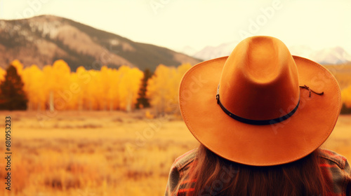 Blonde cowgirl in hat at meadow with mountains on background photo