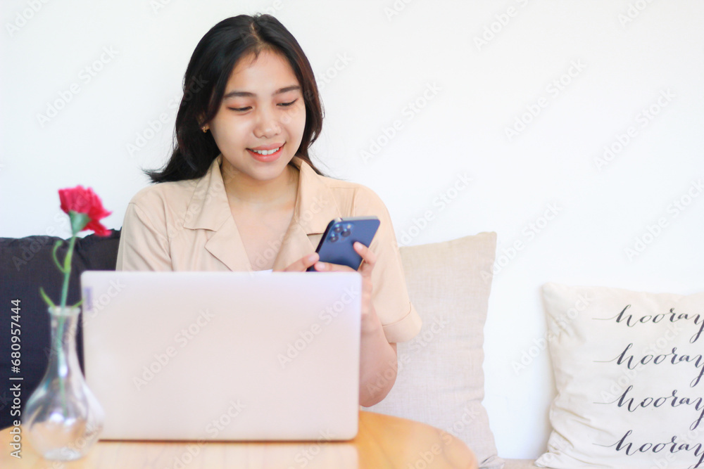 happy asian woman sitting on cozy sofa using smartphone with laptop on wooden table wearing fashionable clothes, female online business owner working at home happy asian woman sitting on cozy sofa using smartphone with laptop on wooden table wearing fashionable clothes, female online business owner working at home