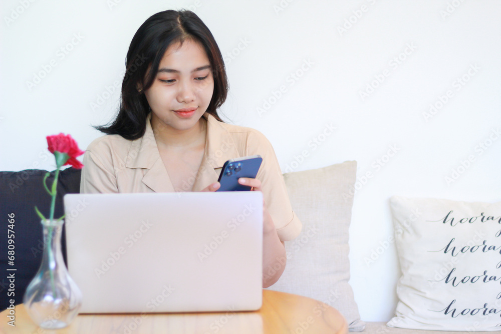 happy asian woman sitting on cozy sofa using smartphone with laptop on wooden table wearing fashionable clothes, female online business owner working at home happy asian woman sitting on cozy sofa using smartphone with laptop on wooden table wearing fashionable clothes, female online business owner working at home