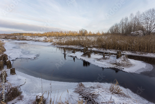 Wooden piles from an old destroyed bridge over the river. Winter landscape with frozen river and blue sky with clouds, nature series