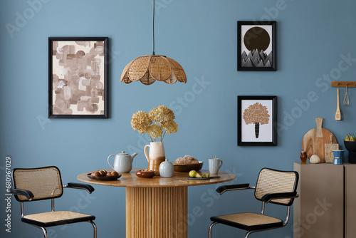 Interior design of cozy dinning room and kitchen interior with mock up poster frame, round table, rattan armchair, beige sideboard, vase with flowers and personal accessories. Home decor. Template.