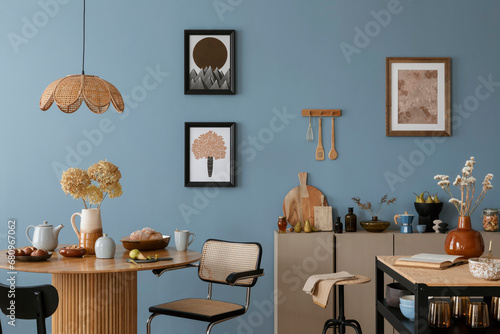 Dinning room and kitchen interior with mock up poster frame, round table, rattan chair, beige commode, vase with dried flowers, cup, pitcher and kitchen accessories. Home decor. Template.