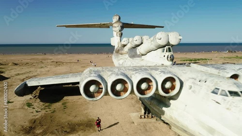 a white ekranoplane is standing on the seashore, on a sandy beach, tourists are walking around, a drone shot, slow motion, flying around the plane, airplane details photo