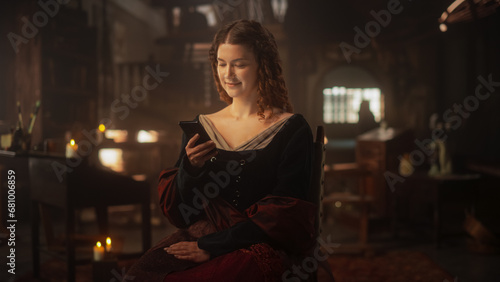 Innovation Concept: Beautiful Female in Medieval Clothes Using Smartphone Indoors. Princess in her Castle Texting Friends, Posting on Social Media, Looking for her Prince Charming on Dating Apps