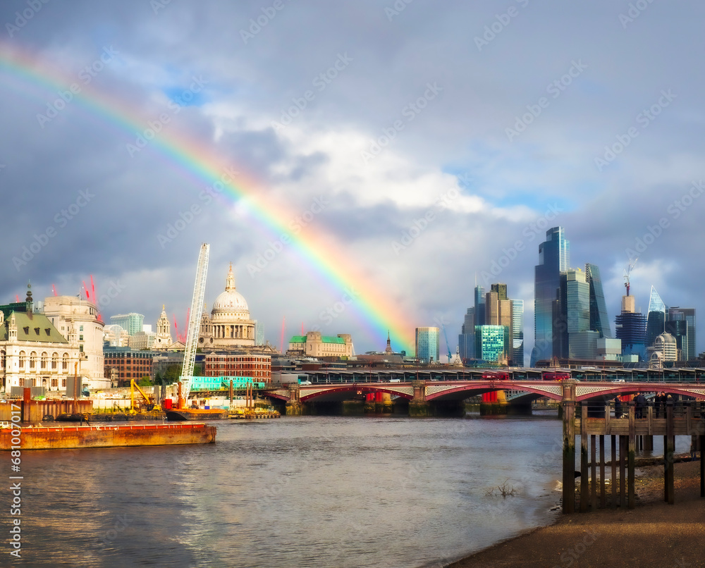 View across the river Thames toward St Pauls Cathedral and city skyscrapers with a rainbow in the sky 