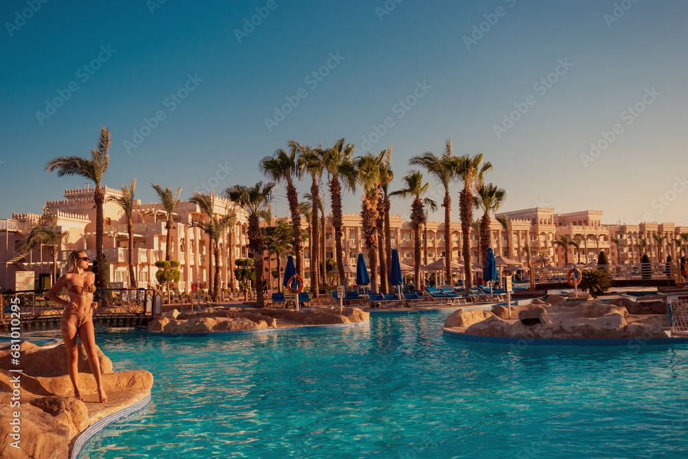 A girl in a swimsuit poses near the pool overlooking the hotel complex in Hurghada - obrazy, fototapety, plakaty 