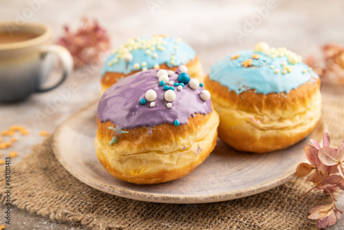 Purple and blue glazed donut and cup of coffee on brown concrete, side view, selective focus.