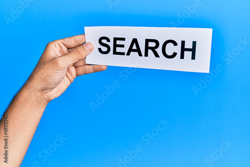 Hand of caucasian man holding paper with search word over isolated blue background