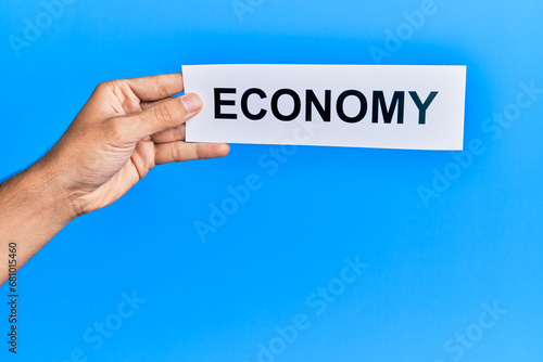 Hand of caucasian man holding paper with economy word over isolated blue background