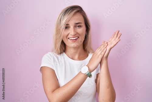 Young blonde woman standing over pink background clapping and applauding happy and joyful, smiling proud hands together