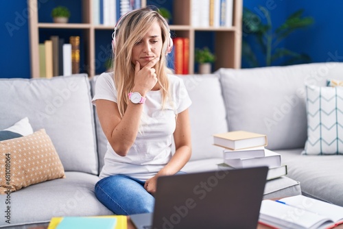 Young blonde woman studying using computer laptop at home looking confident at the camera smiling with crossed arms and hand raised on chin. thinking positive.