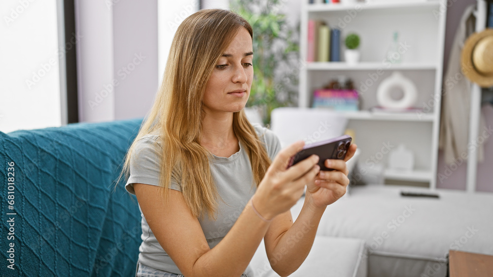 Young blonde woman focused playing video game sitting on sofa at home Young blonde woman focused playing video game sitting on sofa at home
