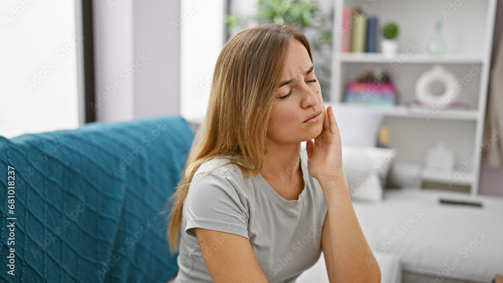 Attractive young blonde adult woman sitting on living room sofa at home, suffering in agony from severe teeth pain - oral issue demanding dentist's help urgently. Attractive young blonde adult woman sitting on living room sofa at home, suffering in agony from severe teeth pain - oral issue demanding dentist's help urgently.