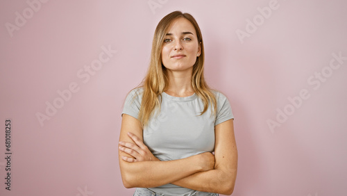 Stunning young blonde woman, all seriousness and resolve, standing with crossed arms over vibrant pink isolated background