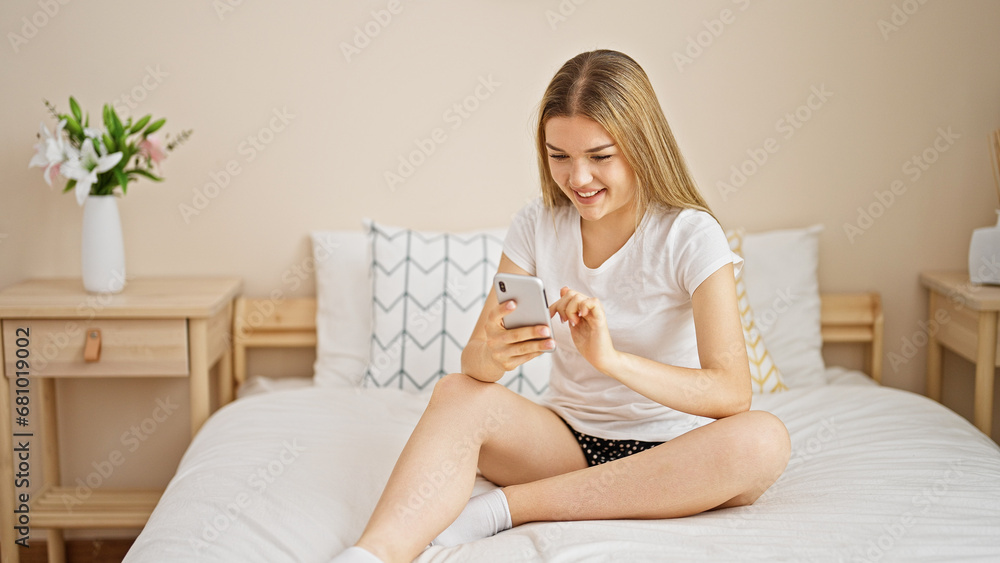 Young blonde woman using smartphone sitting on bed at bedroom Young blonde woman using smartphone sitting on bed at bedroom