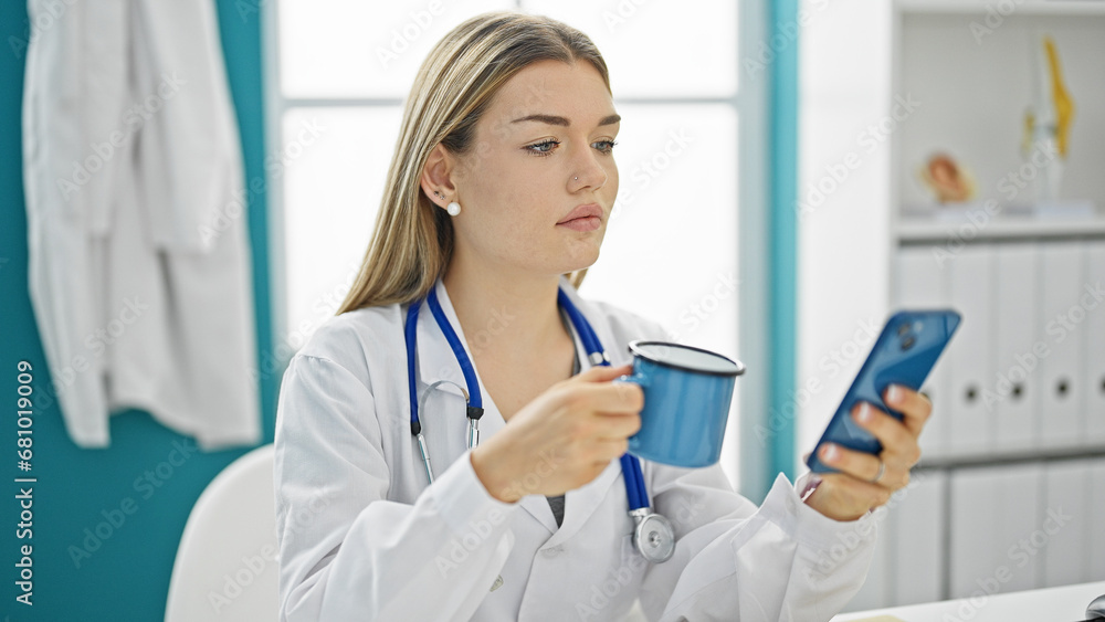 Young blonde woman doctor using smartphone drinking coffee at clinic Young blonde woman doctor using smartphone drinking coffee at clinic