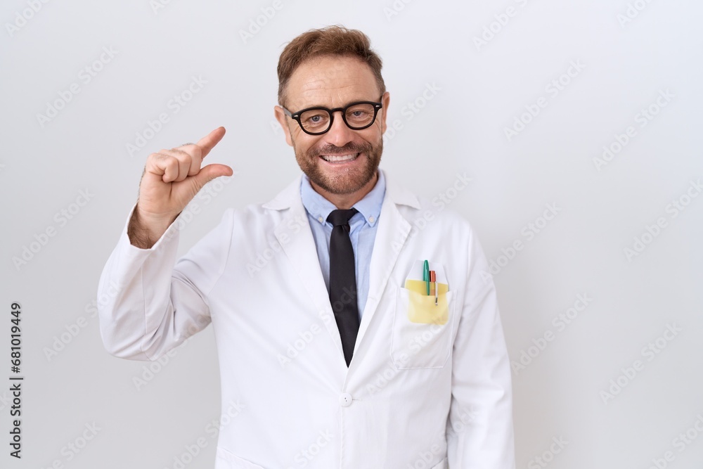 Middle age doctor man with beard wearing white coat smiling and confident gesturing with hand doing small size sign with fingers looking and the camera. measure concept. Middle age doctor man with beard wearing white coat smiling and confident gesturing with hand doing small size sign with fingers looking and the camera. measure concept.