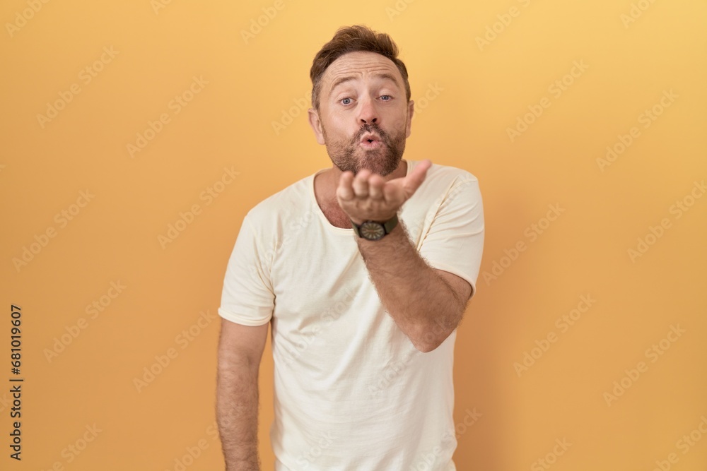 Middle age man with beard standing over yellow background looking at the camera blowing a kiss with hand on air being lovely and sexy. love expression. Middle age man with beard standing over yellow background looking at the camera blowing a kiss with hand on air being lovely and sexy. love expression.