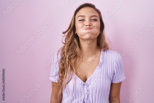 Obraz na plátne Young hispanic woman standing over pink background puffing cheeks with funny face