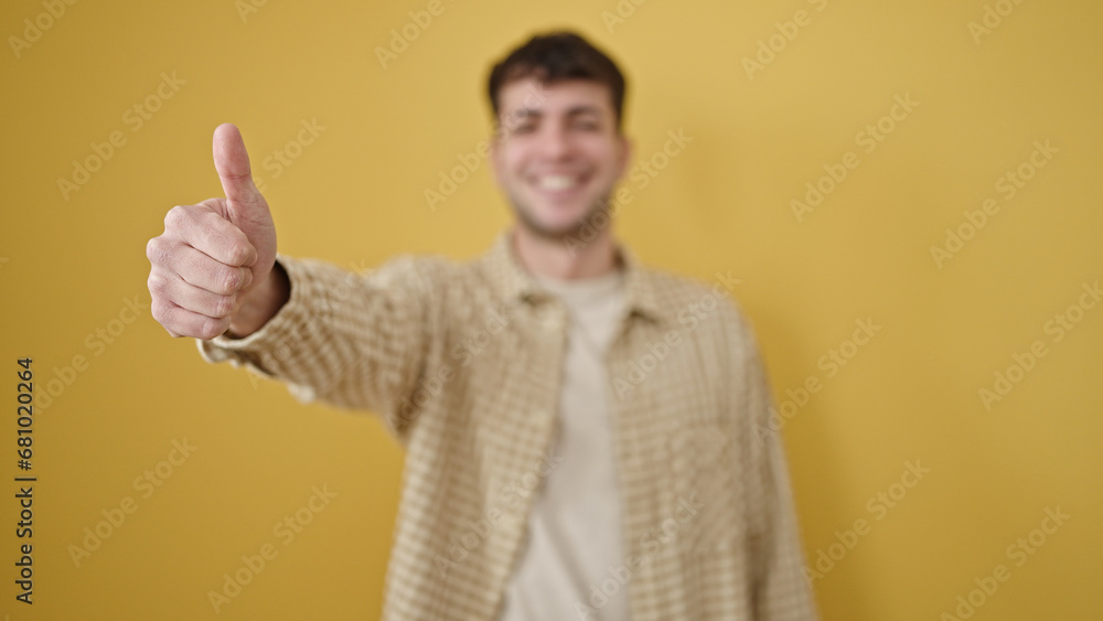 Young hispanic man smiling with thumb up over isolated yellow background Young hispanic man smiling with thumb up over isolated yellow background