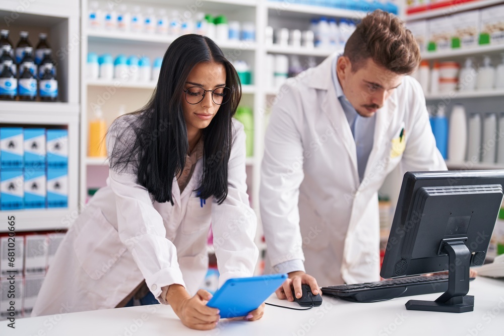 Man and woman pharmacists using touchpad and computer working at pharmacy