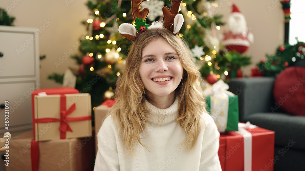 Young blonde woman smiling confident sitting on floor by christmas tree at home