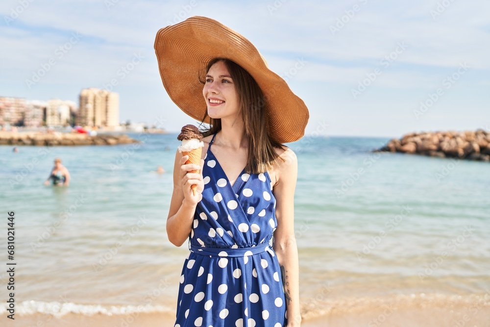 Young blonde woman tourist wearing summer hat holding ice cream at beach