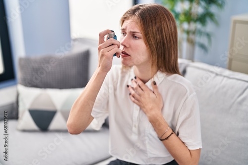 Young blonde woman using inhaler sitting on sofa at home