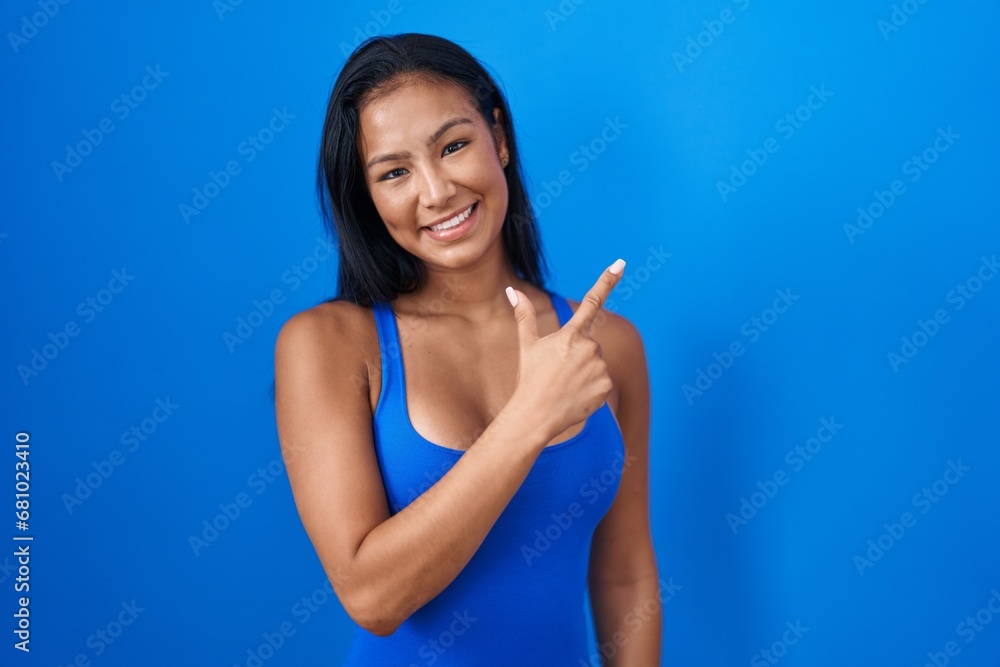 Hispanic woman standing over blue background cheerful with a smile on face pointing with hand and finger up to the side with happy and natural expression Hispanic woman standing over blue background cheerful with a smile on face pointing with hand and finger up to the side with happy and natural expression