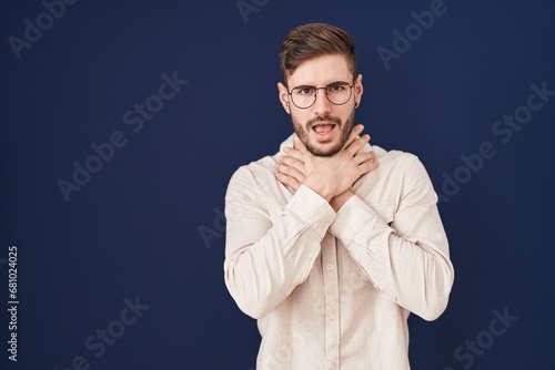 Hispanic man with beard standing over blue background shouting and suffocate because painful strangle. health problem. asphyxiate and suicide concept.