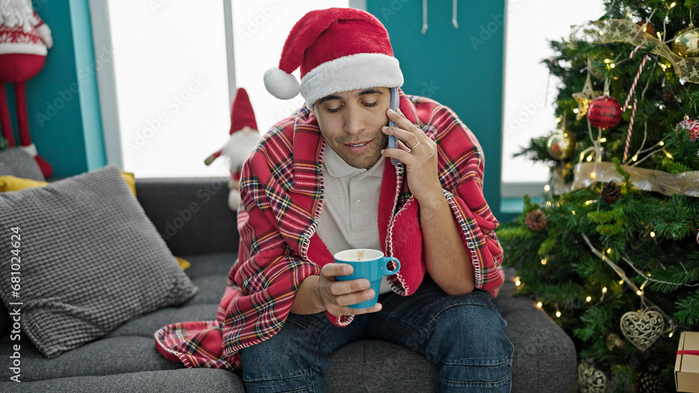 Young hispanic man talking on smartphone drinking coffee celebrating christmas at home Young hispanic man talking on smartphone drinking coffee celebrating christmas at home