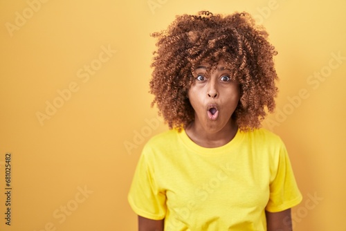 Young hispanic woman with curly hair standing over yellow background afraid and shocked with surprise expression, fear and excited face.