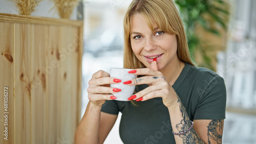 Young blonde woman drinking coffee sitting on table at coffee shop