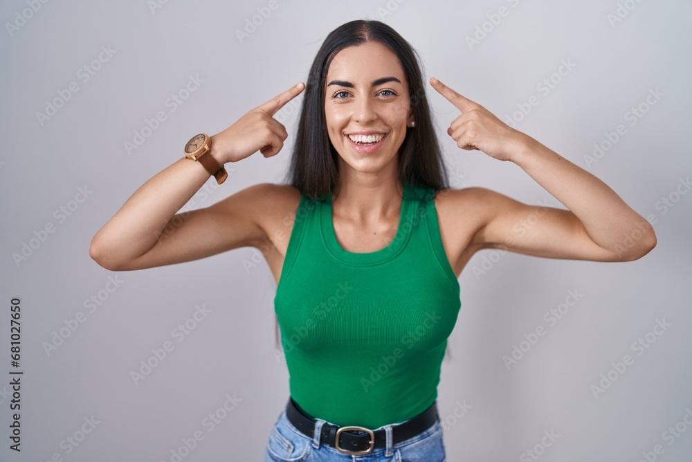 Young woman standing over isolated background smiling pointing to head with both hands finger, great idea or thought, good memory Young woman standing over isolated background smiling pointing to head with both hands finger, great idea or thought, good memory