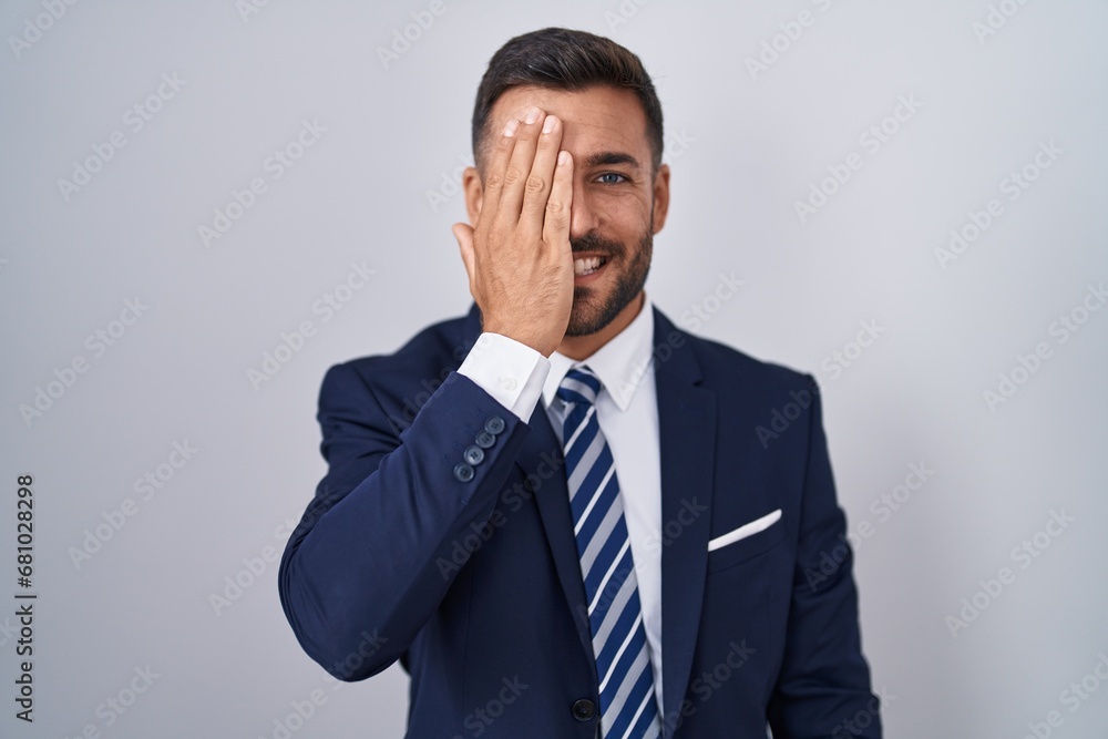 Handsome hispanic man wearing suit and tie covering one eye with hand, confident smile on face and surprise emotion. Handsome hispanic man wearing suit and tie covering one eye with hand, confident smile on face and surprise emotion.