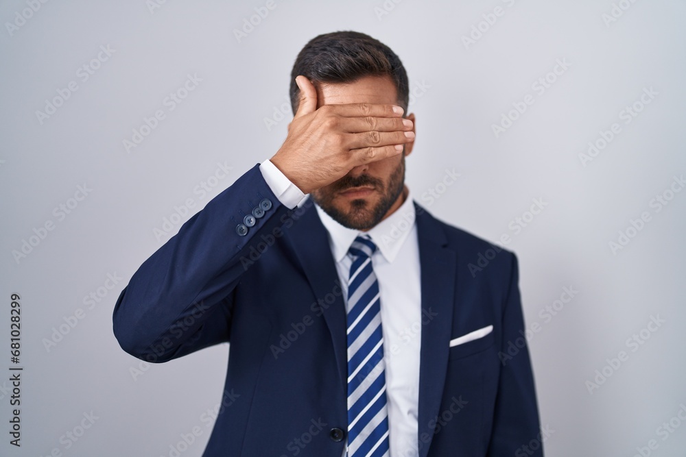Handsome hispanic man wearing suit and tie covering eyes with hand, looking serious and sad. sightless, hiding and rejection concept Handsome hispanic man wearing suit and tie covering eyes with hand, looking serious and sad. sightless, hiding and rejection concept