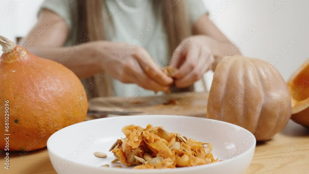 Woman at the Table Transfers Pumpkin Seeds into a White Plate, Close-up. Pumpkins on a Wooden Table, Camera Moving Down. Woman at the Table Transfers Pumpkin Seeds into a White Plate, Close-up. Pumpkins on a Wooden Table, Camera Moving Down.