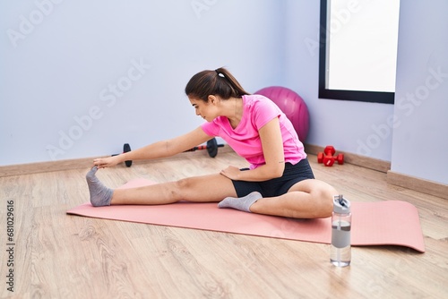 Young beautiful hispanic woman stretching leg at sport center