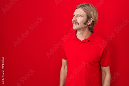 Caucasian man with mustache standing over red background looking away to side with smile on face, natural expression. laughing confident. © Krakenimages.com