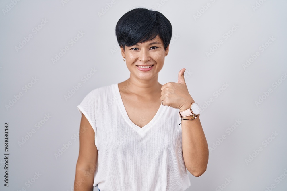 Young asian woman with short hair standing over isolated background doing happy thumbs up gesture with hand. approving expression looking at the camera showing success. Young asian woman with short hair standing over isolated background doing happy thumbs up gesture with hand. approving expression looking at the camera showing success.