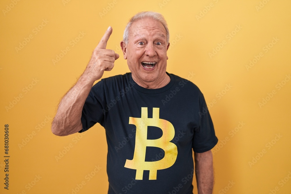 Φωτογραφία Senior man with grey hair wearing bitcoin t shirt smiling amazed and surprised and pointing up with fingers and raised arms