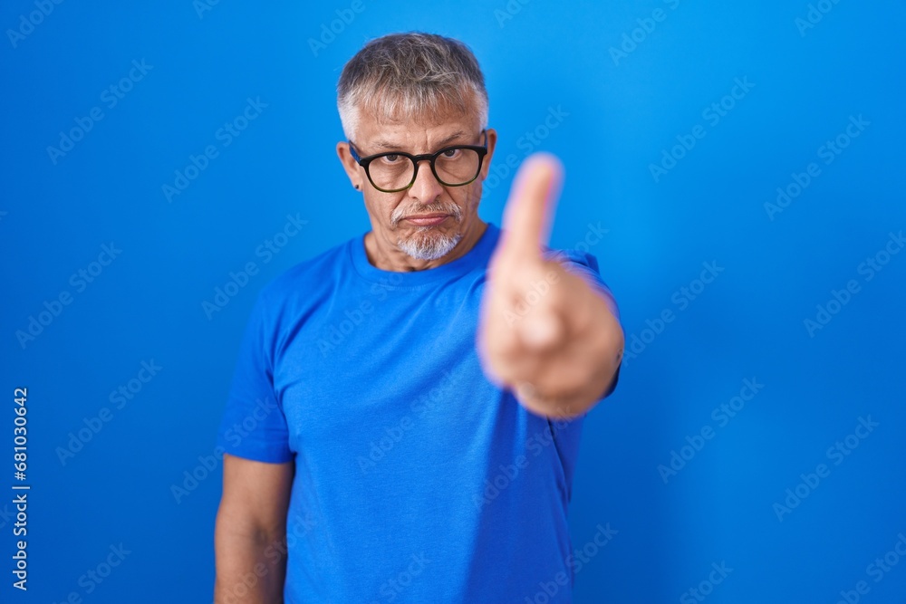 Hispanic man with grey hair standing over blue background pointing with finger up and angry expression, showing no gesture Hispanic man with grey hair standing over blue background pointing with finger up and angry expression, showing no gesture