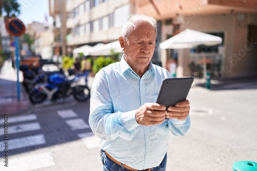 Middle age grey-haired man using touchpad with serious expression at street