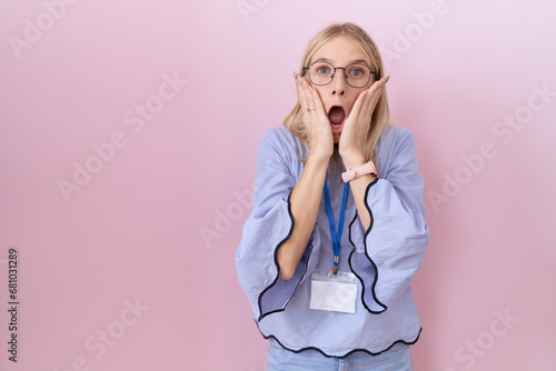 Young caucasian business woman wearing id card afraid and shocked, surprise and amazed expression with hands on face