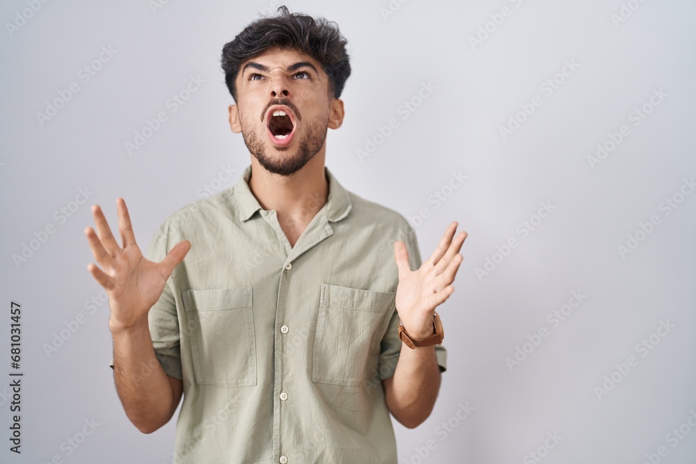 Arab man with beard standing over white background crazy and mad shouting and yelling with aggressive expression and arms raised. frustration concept. Arab man with beard standing over white background crazy and mad shouting and yelling with aggressive expression and arms raised. frustration concept.